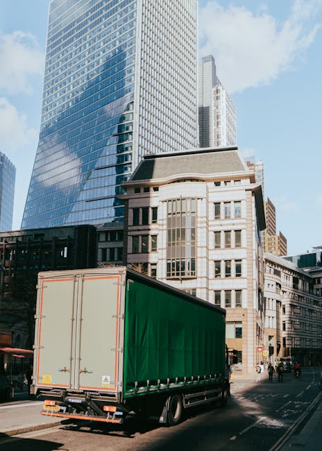 A red double-decker bus in motion on a city street in front of a large, historic white stone building with ornate architectural details and tall windows. The bus appears blurred due to movement, indic